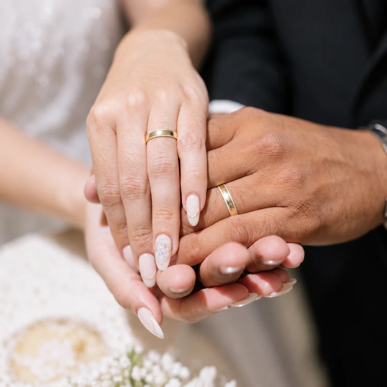Manos entrelazadas de una pareja con alianzas de acabado dorado