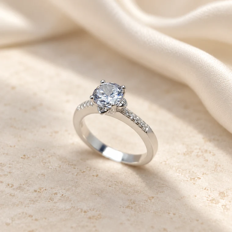 Anillo solitario de acabado plateado con una piedra transparente sobre una superficie clara y seda